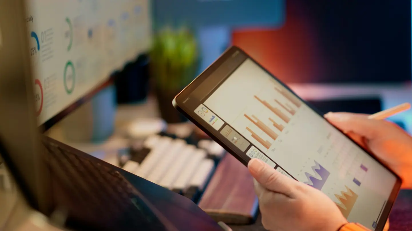 Pessoa analisando dados em um tablet e computador